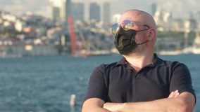 Video, an adult man in a white shirt and sunglasses in a protective mask. On a sunny day in summer, against the backdrop of the turquoise sea and sailing ships.