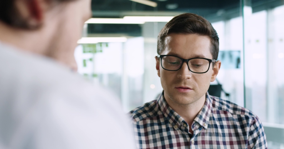 Close up portrait of handsome male patient in glasses having conversation with doctor in hospital on medical consultation. Coronavirus pandemic. Doctor appointment. Over shoulder view. Clinic concept | Shutterstock HD Video #1063251916