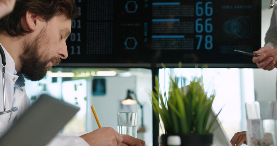 Close up of multi-ethnic diverse doctors looking at digital display presentation sitting at conference and discussing statistics of covid-19. Coronavirus pandemic. Hospital concept