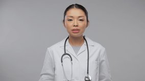 medicine, profession and healthcare concept - portrait of happy smiling asian female doctor in white coat with stethoscope having video call or online consultation over grey background