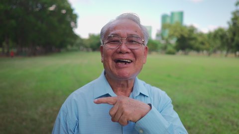 Asian Senior waving hands to say hello to camera and introduce self. Smart old man talking to camera happily.