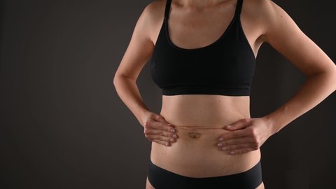 Cropped view of woman in black underwear massages her flabby belly with her hands, isolated on grey. Skin care and wight loss concept.