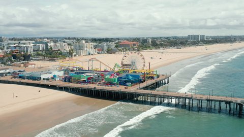 Santa Monica Pier on cloudy day, Los Angeles. The footage of the Santa Monica pier and the amusement park from the side of the ocean. Beautiful panorama of the city skyline is seen behind sandy beach