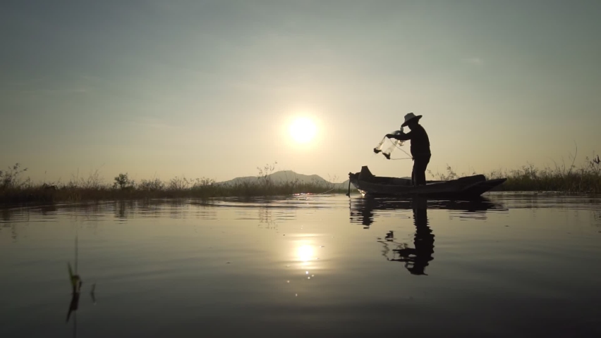 Footage B roll Slow Motion Full HD format of Silhouette fisherman throwing fishing net during sunset with boats at the lake. Traditional culture of Thailand. Concept Fisherman's life style. Royalty-Free Stock Footage #1063263127