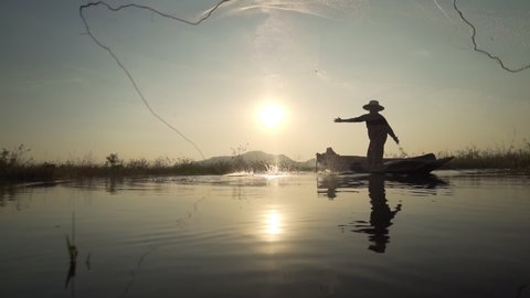 Footage B roll Slow Motion Full HD format of Silhouette fisherman throwing fishing net during sunset with boats at the lake. Traditional culture of Thailand. Concept Fisherman's life style.