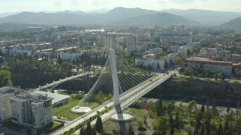 Aerial shot Podgorica Montenegro. Drone video Millennium Bridge standing surrounded by houses and streets, where you can see the mountains in the background, the river and the beautiful landscape.