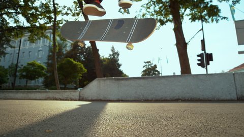 SLOW MOTION TIME WARP, LENS FLARE, CLOSE UP, LOW ANGLE, DOF: Skateboarder lands a nollie kickflip during freestyle session at an urban skate park. Unrecognizable man lands a trick while skateboarding