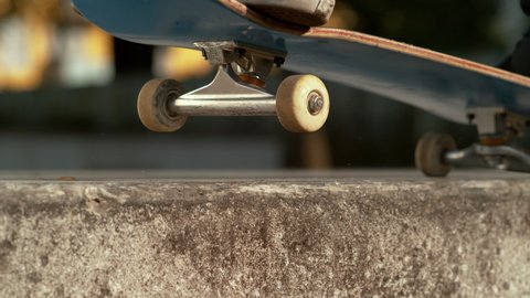 SLOW MOTION TIME WARP, CLOSE UP, DOF: Skater skilfully does a manual along the edge of a concrete ledge. Detailed shot of a balance trick done by unrecognizable skateboarder riding around the city.