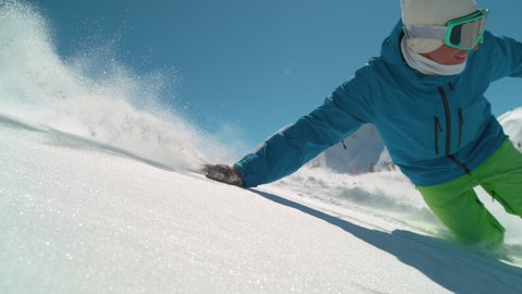SLOW MOTION TIME WARP, CLOSE UP, DOF: Snowboarder drags his hand along the fresh blanket of powder snow while riding off trail in the scenic Alps. Cinematic shot of male snowboarder shredding slopes.