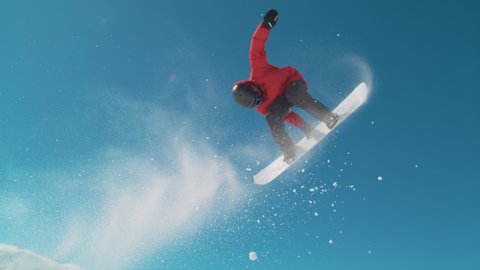 SLOW MOTION TIME WARP, CLOSE UP: Extreme snowboarder does a cool spinning big air trick on sunny winter day. Active tourist snowboarding in the Alps rides off a kicker and performs a spinning grab.