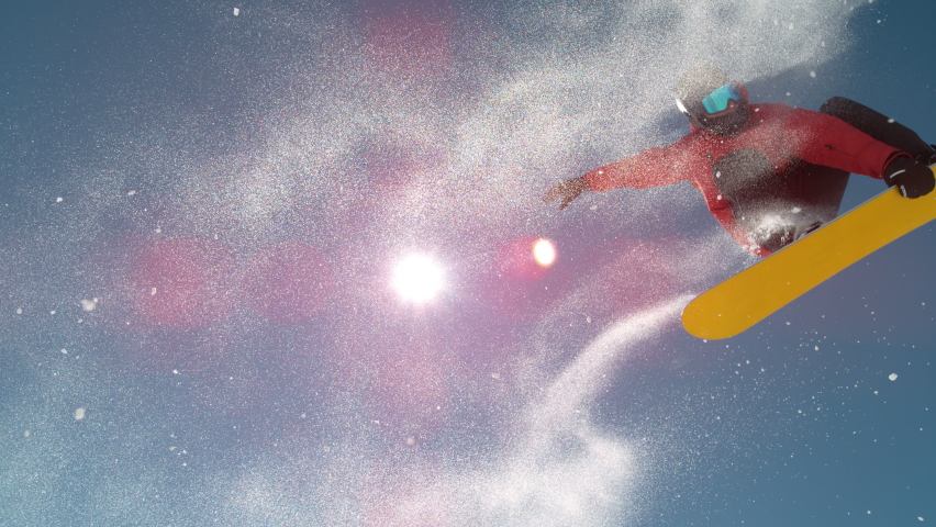 SLOW MOTION TIME WARP, LENS FLARE, CLOSE UP: Fearless snowboarder does a spin trick while riding off a big air kicker. Snowflakes sparkle in the sunshine as male tourist does snowboarding tricks.