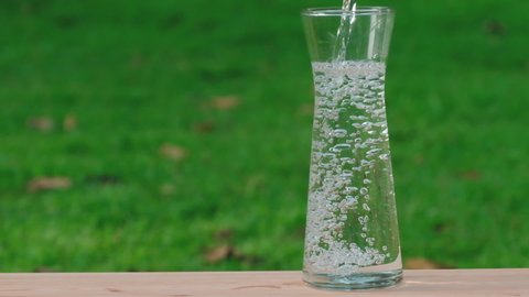 Pouring pure water in to the glass bottle make spread of water crystal bubble on green grass background