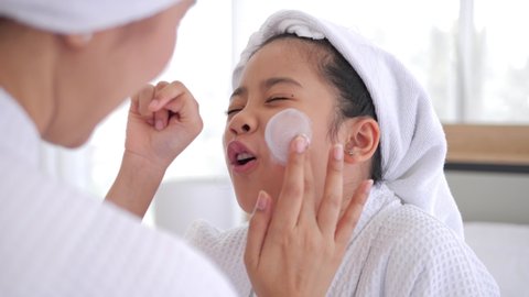 Mother applying blemish cream on her daughter face relaxing in the bedroom after shower. Family beauty treatment. Teenage skin problems.