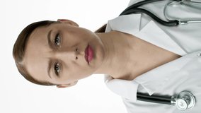 vertical shot Attractive female therapist in medical coat with stethoscope over neck is very surprised, opens her mouth, holds her chin and scratches her head. Doctor reaction concept. Isolated on