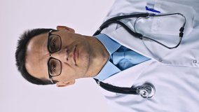 vertical shot Middle aged caucasian doctor wearing white medical coat with stethoscope over neck and eyeglasses. Puts on a protective sterile medical mask. Virus protection concept. Isolated. Studio