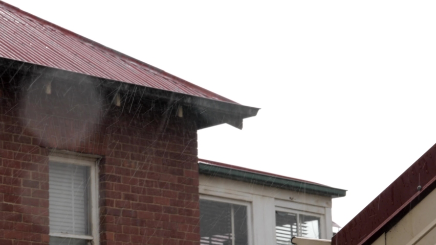 Rain pouring down in residential area in front of red and white brick house with water on lens