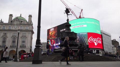 London , United Kingdom (UK) - 03 17 2020: A woman wearing a face mask walks past Eros Statue and the neon billboard at Piccadilly Circus