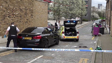 London , United Kingdom (UK) - 03 18 2020: A police officer searches a black car while another takes a witness statement at the scene of a stabbing incident