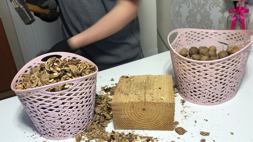 A man pricks walnuts with a hammer. On a wooden block. Nuts are in the basket.