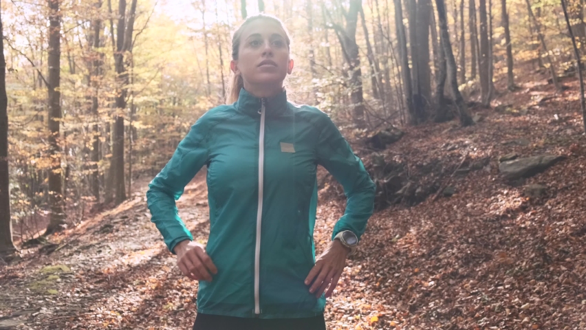 Female jogger standing in autumn forest, looking around