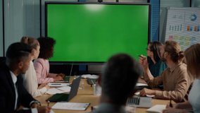 Multi ethnic business team looking at presentation on big tv with green screen in office. Business people having online video conference during quarantine. Coworkers working in meeting room together