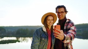 Portrait attractive young couple use phone and take selfie have video call in the forest near lake. Nature mobile relationship. Outdoors. Romantic. Close up. Slow motion
