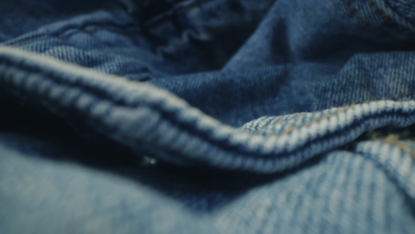 Macro shot of blue denim jeans material. Slider dolly extreme close-up of clothing material fabric texture. Seams sewn with yellow threads. Shot with laowa 24mm lens Royalty-Free Stock Footage #1063289917