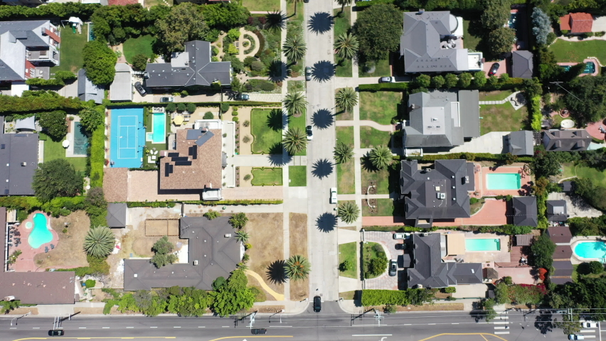 Drone shot flying over beauitufl palm tree lined streets with silver, white and black cars driving, the streets surrounded by mansions with swimming pools in West Hollywood, Los Angeles, California Royalty-Free Stock Footage #1063290394