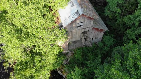 Aerial of water stream and old barn in lush green forest on sunny day