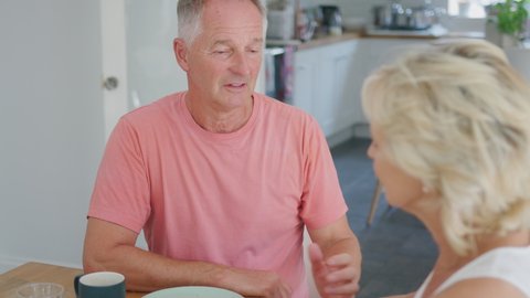 Retired senior couple at home around breakfast with woman comforting man suffering with depression - shot in slow motion