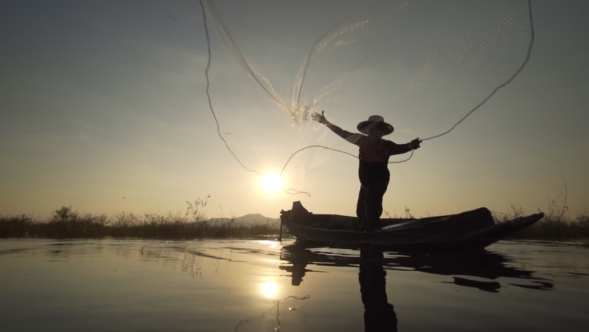 Footage B roll Slow Motion Full HD format of Silhouette fisherman throwing fishing net during sunset with boats at the lake. Traditional culture of Thailand. Concept Fisherman's life style. | Shutterstock HD Video #1063295488