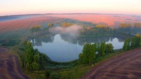 4K aerial - a bird's eye view video (Ultra High Definition). Summer sunrise on Ternopil outskirts with lake and asphalt road. Foggy morning view of hte Ukrainian countryside with field of wheat.