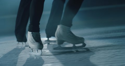 Cinematic close up shot of couple figure skaters skating shoes while performing a woman's single choreography on ice rink during a competition. Concept of perfection, precision, freedom, passion.
