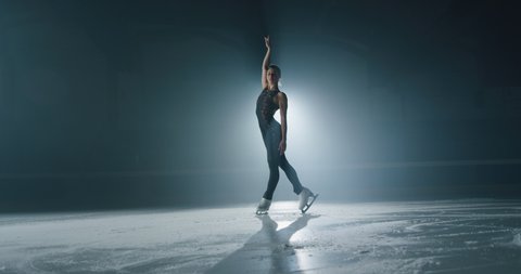 Cinematic shot of young female artistic figure skater is performing a woman's single skating choreography on ice rink before start of a competition. Concept of perfection, precision, freedom, passion.