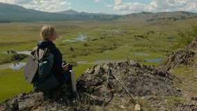 Young tourist taking a photo sitting on the top of a mountain. Summer video shooting in the Altai mountains, Russia. 4K, HD