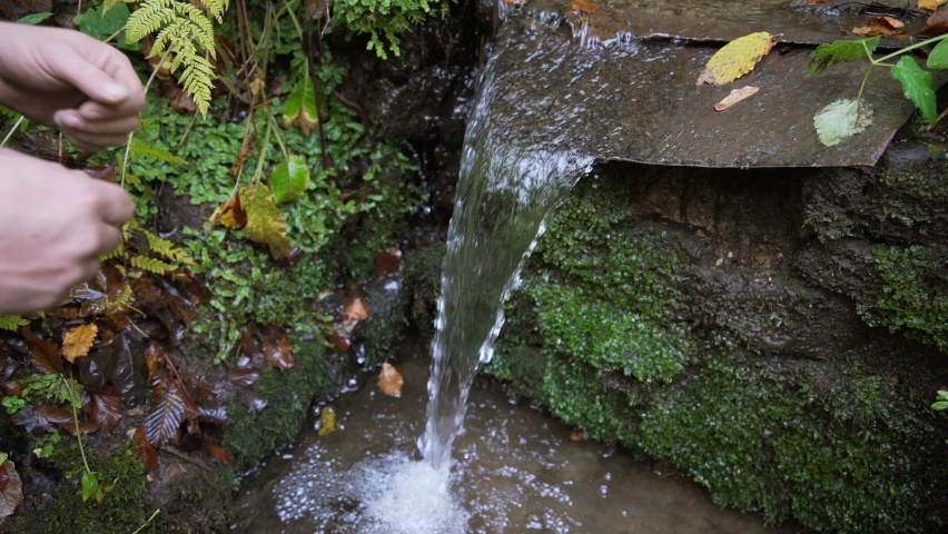 Man in black hoodie is washing his hands in a creek