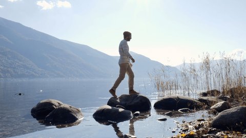 Man jumping from rock to rock on the lake shore 