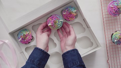 Time lapse. Flat lay. Step by step. Boxing unicorn chocolate cupcakes into a white cupcake box.