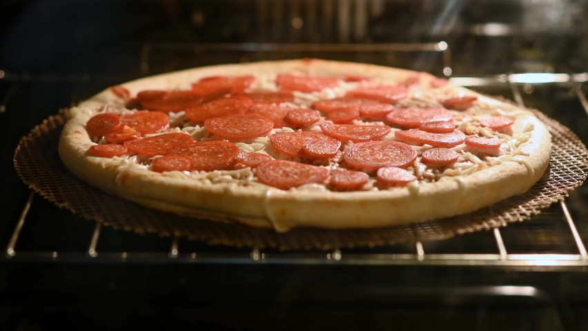 ZOOM IN Time lapse of pepperoni pizza cooking in an oven. The pepperoni slowly curls as it cooks and the cheese bubbles and browns. | Shutterstock HD Video #1063304068