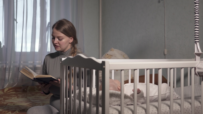 Tired mom reads a book near the crib of a newborn baby. Family, maternity theme. Royalty-Free Stock Footage #1063304140