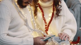 Happy young couple congratulates parents on Christmas using video call at home. Arabic man and Caucasian woman are looking at the screen of a smartphone and gesturing happily. Close-up.