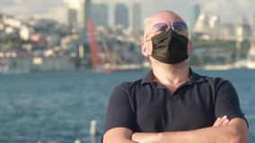 Video, an adult man in a white shirt and sunglasses in a protective mask. On a sunny day in summer, against the backdrop of the turquoise sea and sailing ships.