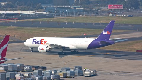 SYDNEY, AUSTRALIA - 2020: FedEx Boeing 777-FS2 Freighter Cargo Jet Airplane Taxiing and Arriving to Logistics Center with Qantas 767 at Sydney SYD Kinsford Smith International Airport on a Sunny Day