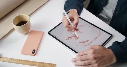 Lviv, Ukraine - May 28, 2020: Male web designer creating sketch of apple on digital tablet.Talanted guy using pad and stylus while sitting and working on illustration at his desk.