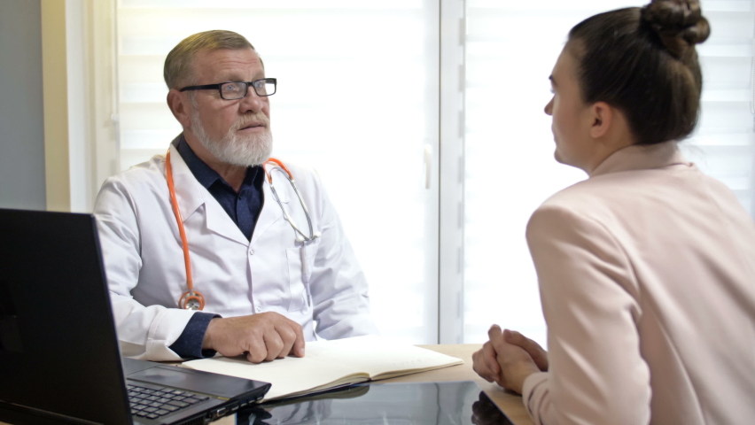 An experienced elderly doctor is consulting a female patient. | Shutterstock HD Video #1063312423