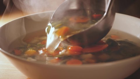 Pour a ladle of minestrone soup. Vegetarian soup dish is on table. Vegetarian healthy meal for dinner. Ready vegetable meal for lunch, hot and cozy soup for dinner at home. Soup with potatoes, carrots