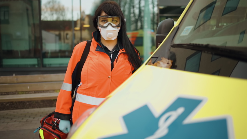 Dolly in: Tired female paramedic posing at ambulance vehicle near hospital