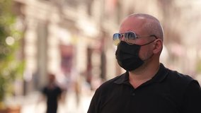 Video, an adult man in a black shirt and sunglasses in a protective black mask. On a sunny day in summer on a city street with lights.