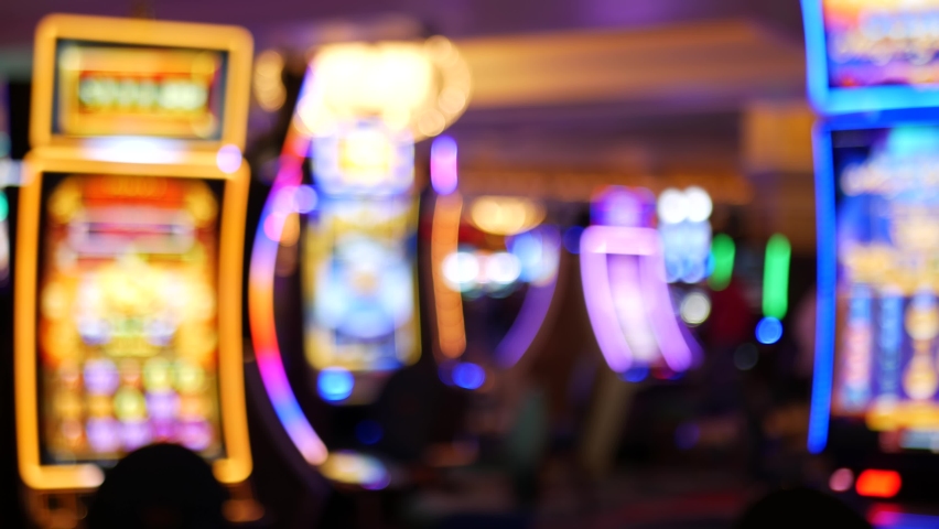 Defocused slot machines glow in casino on fabulous Las Vegas Strip, USA. Blurred gambling jackpot slots in hotel near Fremont street. Illuminated neon fruit machine for risk money playing and betting. | Shutterstock HD Video #1063322422