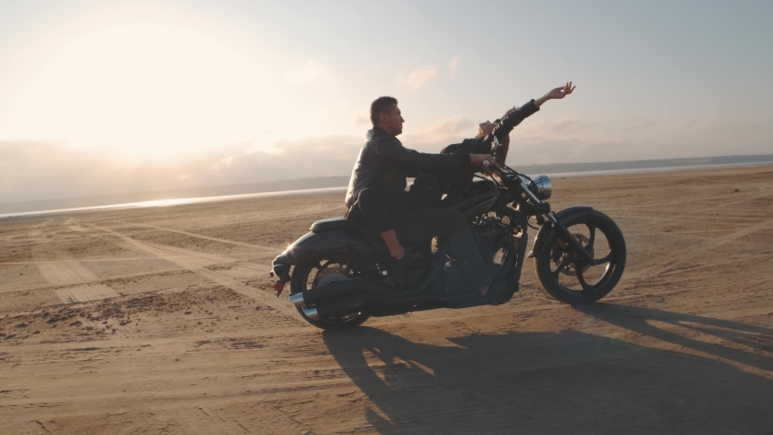 Guy with a girl on a motorcycle in the desert. Couple riding on vintage motorcycle and having a good time at sunset on a dry salt lake. Slow motion shot | Shutterstock HD Video #1063324792
